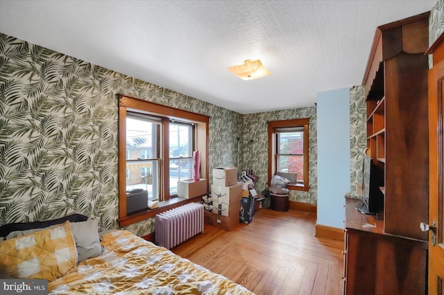 bedroom with parquet floors, radiator heating unit, multiple windows, and a textured ceiling