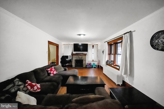 living room featuring hardwood / wood-style floors, ornamental molding, a stone fireplace, and radiator heating unit