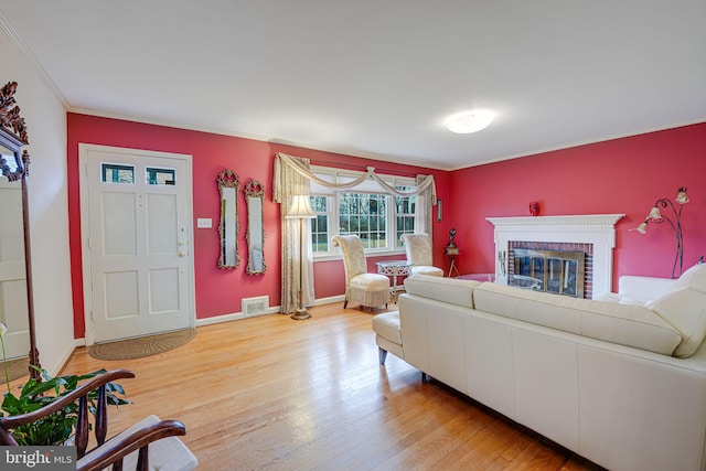 living room featuring ornamental molding, a brick fireplace, and light hardwood / wood-style floors