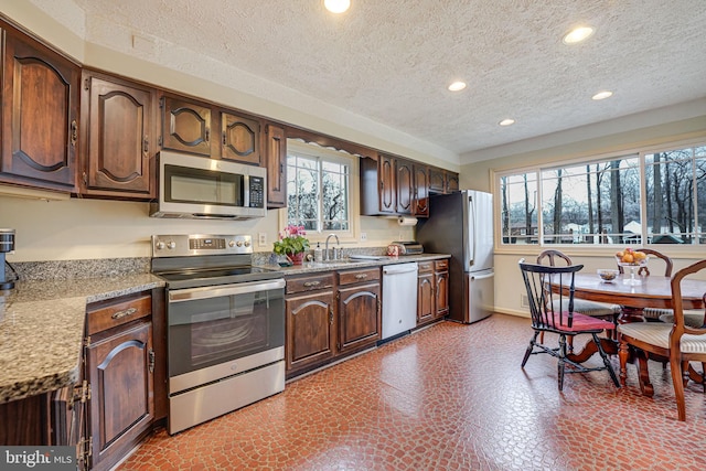 kitchen with sink, dark brown cabinets, a textured ceiling, stainless steel appliances, and light stone countertops