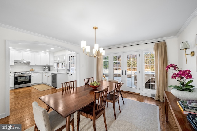 dining area featuring sink, crown molding, light hardwood / wood-style flooring, an inviting chandelier, and french doors