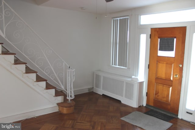 foyer entrance featuring ceiling fan, radiator, and dark parquet floors