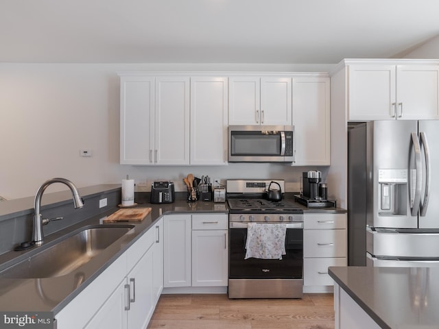 kitchen with light wood-type flooring, appliances with stainless steel finishes, sink, and white cabinets