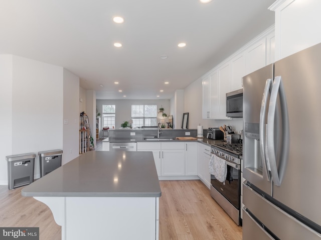 kitchen featuring sink, appliances with stainless steel finishes, white cabinetry, a kitchen island, and kitchen peninsula