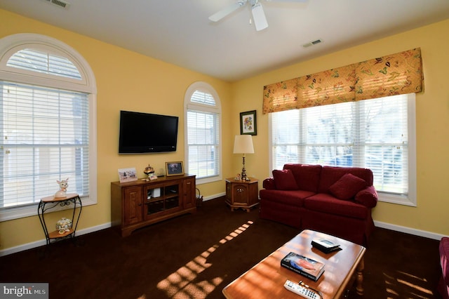 living room featuring a healthy amount of sunlight, ceiling fan, and dark carpet