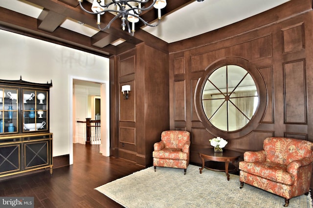 living area featuring dark wood-type flooring, wooden walls, beam ceiling, and an inviting chandelier