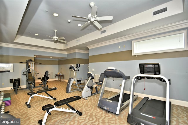 exercise room with ceiling fan, light colored carpet, ornamental molding, and a tray ceiling