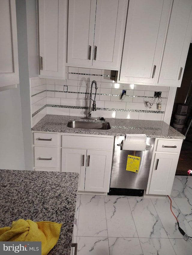 kitchen featuring sink, dishwashing machine, backsplash, white cabinets, and light stone counters