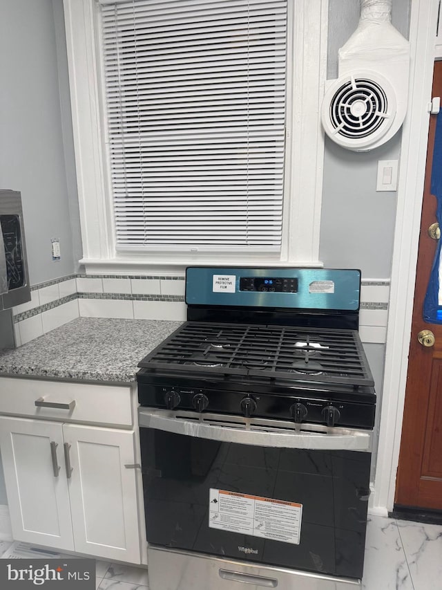 kitchen featuring backsplash, light stone countertops, gas stove, and white cabinets