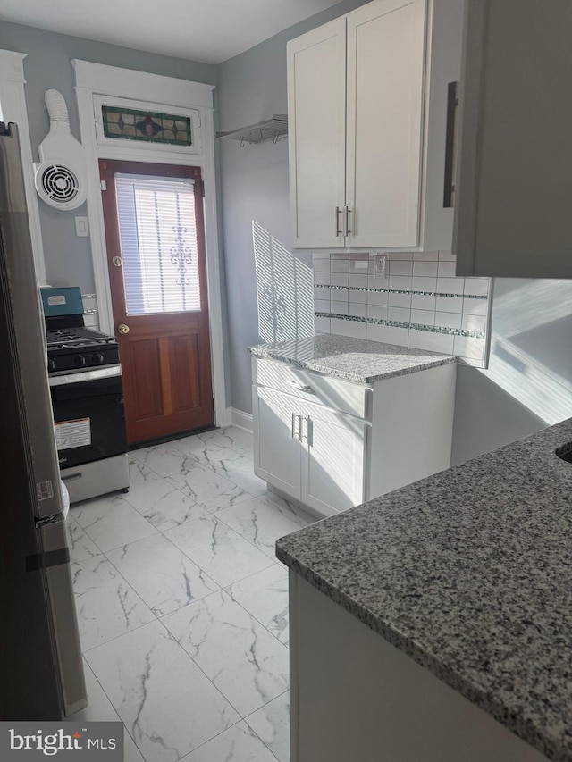 kitchen featuring white cabinetry, appliances with stainless steel finishes, stone countertops, and backsplash