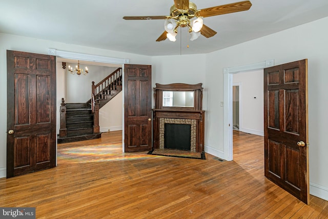 unfurnished living room with ceiling fan with notable chandelier and light hardwood / wood-style floors