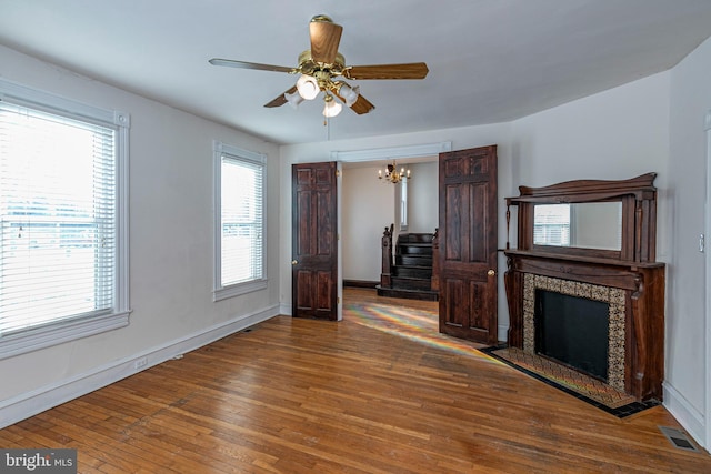 unfurnished living room featuring hardwood / wood-style flooring, a fireplace, and ceiling fan with notable chandelier