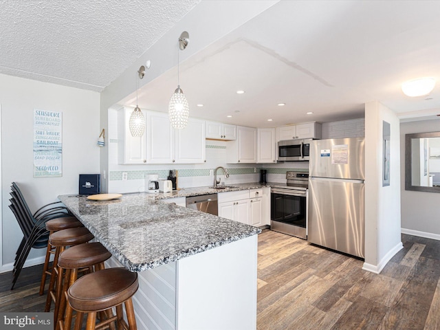 kitchen with white cabinetry, sink, hanging light fixtures, kitchen peninsula, and stainless steel appliances