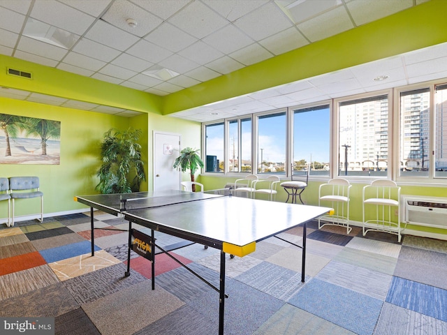 game room featuring a paneled ceiling, carpet, and an AC wall unit