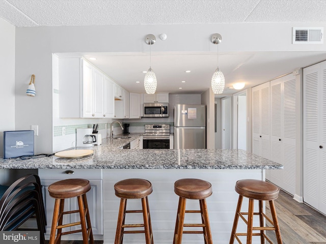 kitchen featuring appliances with stainless steel finishes, light hardwood / wood-style floors, white cabinets, a kitchen bar, and kitchen peninsula