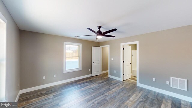 unfurnished bedroom with ensuite bathroom, dark hardwood / wood-style flooring, and ceiling fan