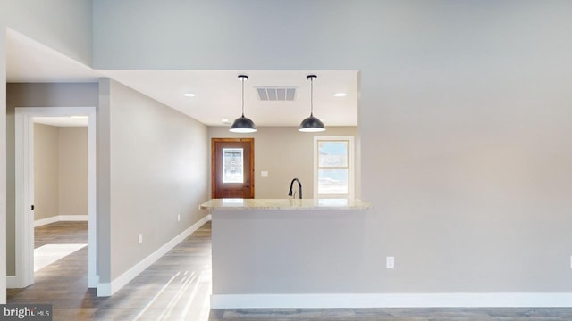 kitchen with sink, light stone counters, kitchen peninsula, pendant lighting, and hardwood / wood-style floors