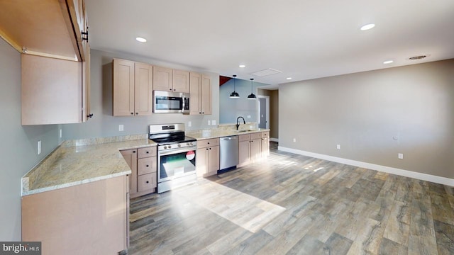 kitchen with appliances with stainless steel finishes, hardwood / wood-style floors, sink, hanging light fixtures, and light stone counters