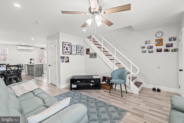 living room featuring a wall unit AC, light hardwood / wood-style floors, and ceiling fan