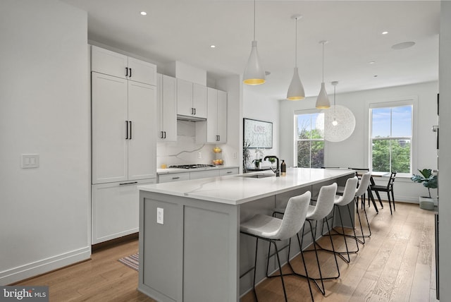 kitchen with an island with sink, sink, white cabinets, hanging light fixtures, and stainless steel gas cooktop