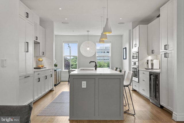 kitchen featuring a breakfast bar, sink, decorative light fixtures, a center island with sink, and white cabinets