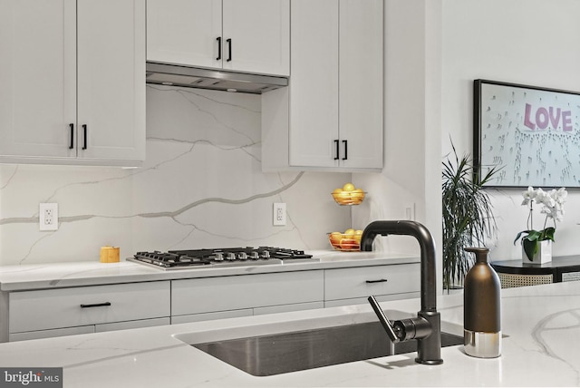 kitchen with sink, white cabinetry, tasteful backsplash, light stone counters, and stainless steel gas cooktop