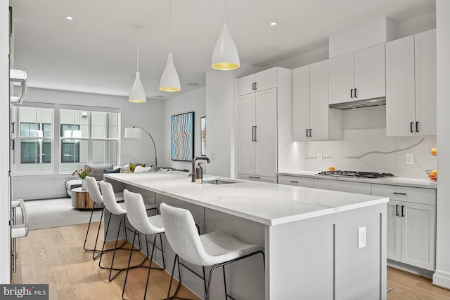 kitchen featuring white cabinetry, an island with sink, light stone counters, and decorative backsplash