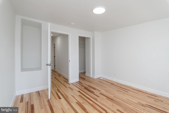 unfurnished bedroom with light wood-style flooring, visible vents, baseboards, and a closet