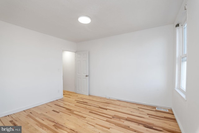 spare room with wood finished floors, visible vents, and baseboards