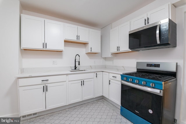 kitchen with white cabinetry, light stone counters, appliances with stainless steel finishes, and a sink