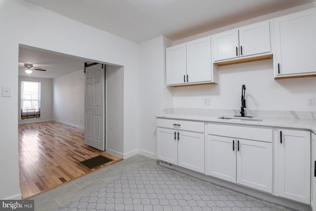 kitchen featuring light stone countertops, a barn door, white cabinets, a ceiling fan, and a sink