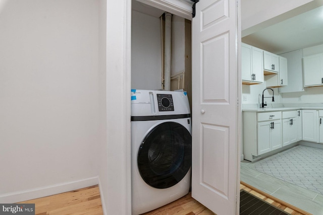 clothes washing area featuring washer / dryer, light wood-type flooring, baseboards, and a sink