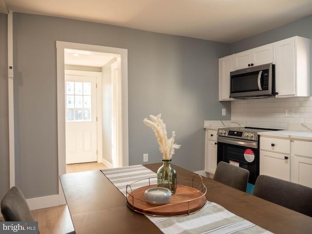 kitchen featuring tasteful backsplash, appliances with stainless steel finishes, light hardwood / wood-style floors, and white cabinets