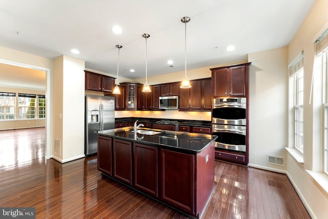 kitchen featuring sink, appliances with stainless steel finishes, dark hardwood / wood-style floors, an island with sink, and pendant lighting