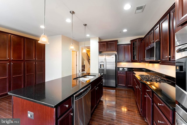 kitchen featuring pendant lighting, sink, dark wood-type flooring, appliances with stainless steel finishes, and a kitchen island with sink