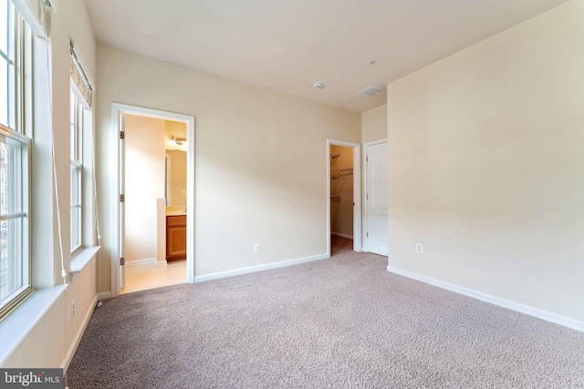 unfurnished bedroom with a walk in closet, light carpet, connected bathroom, and a closet