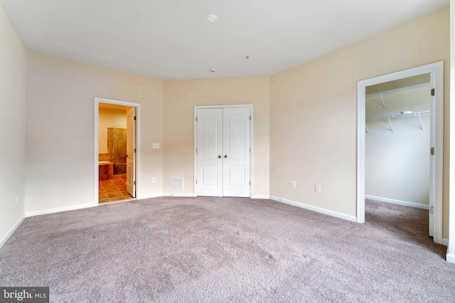 unfurnished bedroom with light colored carpet, ensuite bathroom, and a walk in closet