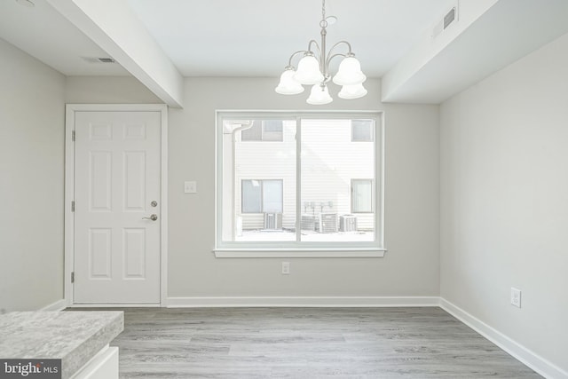 unfurnished dining area with a chandelier, light hardwood / wood-style floors, and a wealth of natural light