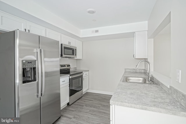 kitchen featuring appliances with stainless steel finishes, sink, light hardwood / wood-style flooring, and white cabinets