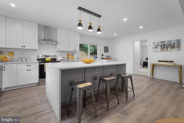 kitchen with a kitchen bar, white cabinetry, stainless steel electric range, a kitchen island, and wall chimney range hood