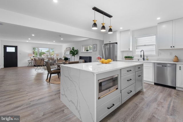 kitchen with pendant lighting, sink, appliances with stainless steel finishes, white cabinetry, and a center island