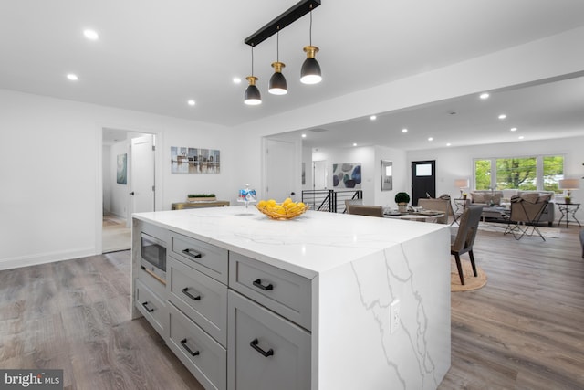 kitchen featuring a kitchen island, stainless steel microwave, decorative light fixtures, wood-type flooring, and light stone countertops