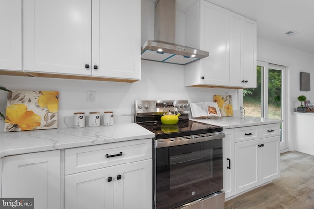 kitchen with stainless steel electric stove, white cabinets, light wood-type flooring, and wall chimney exhaust hood