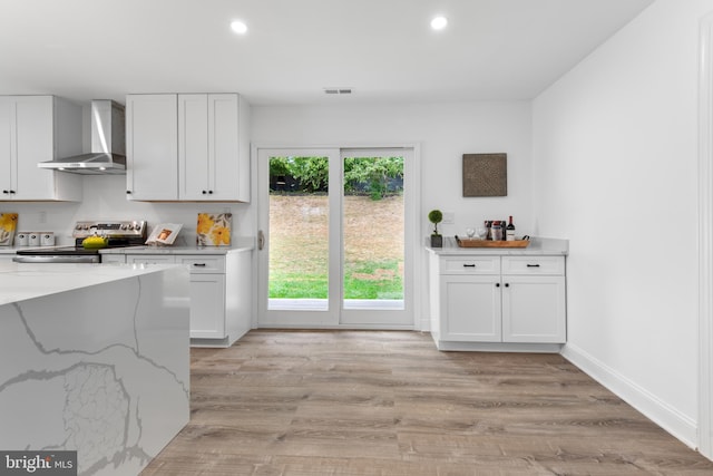 kitchen with stainless steel electric range oven, white cabinetry, light hardwood / wood-style floors, light stone countertops, and wall chimney range hood