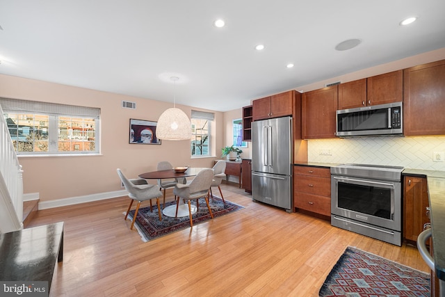 kitchen featuring pendant lighting, stainless steel appliances, light hardwood / wood-style flooring, and backsplash