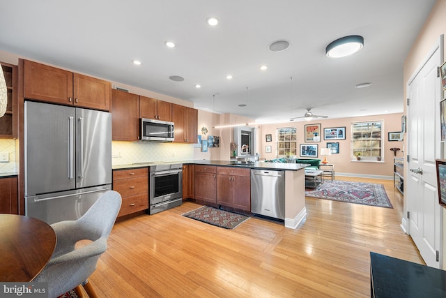 kitchen featuring sink, backsplash, premium appliances, kitchen peninsula, and light wood-type flooring