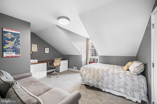 bedroom with built in desk, lofted ceiling, and light carpet