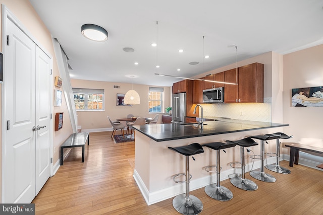 kitchen with a breakfast bar, sink, tasteful backsplash, hanging light fixtures, and appliances with stainless steel finishes