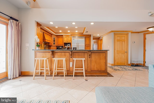 kitchen with built in appliances, a tray ceiling, custom range hood, light tile patterned flooring, and kitchen peninsula