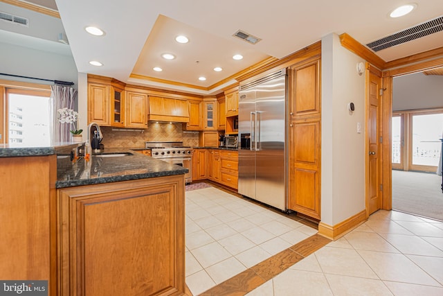 kitchen featuring sink, light tile patterned floors, premium appliances, kitchen peninsula, and decorative backsplash